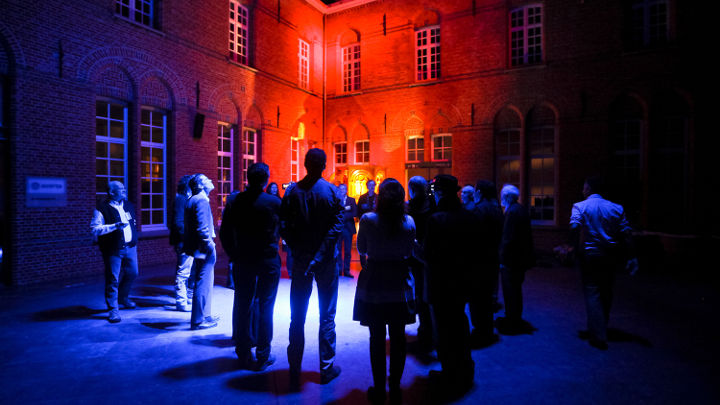 Veľká skupina ľudí diskutuje pred pekne osvetlenou budovou v meste Turnhout v Belgicku na workshope organizovanom spoločnosťou Philips.