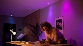 Inteligentné LED svetlá Philips Hue vytvárajú žiarivú fialovú a ružovú atmosféru v obývacej izbe a predstavujú prispôsobiteľné náladové osvetlenie pre filmové večery a relaxáciu v moderných domácnostiach.